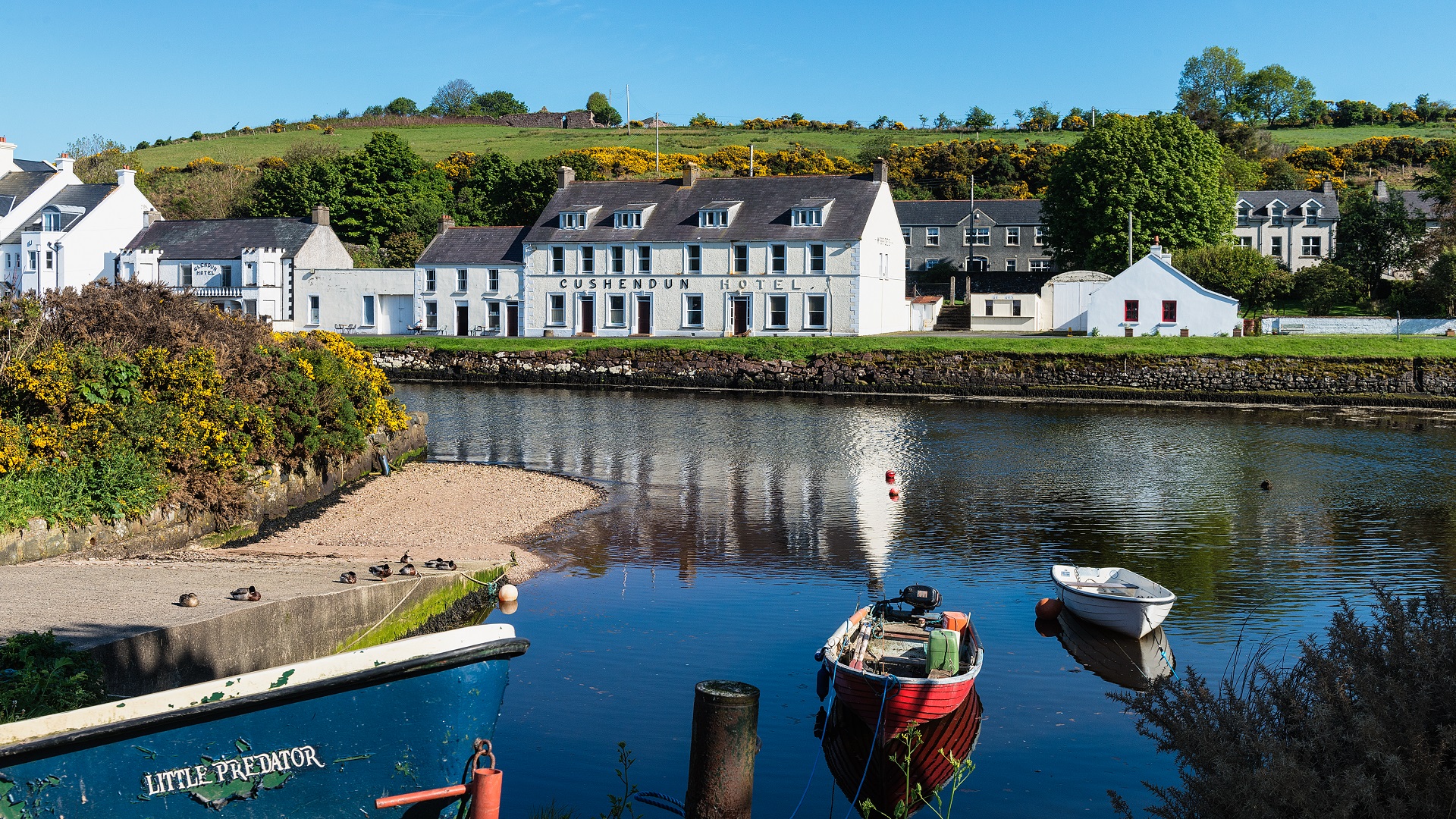 A view of Cushendun's small harbour and bay, with fishing boats and coastal homes along the water's edge.